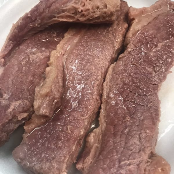 Close-up of several pieces of cooked Polynesian-style beef, glistening with moisture on a white surface.