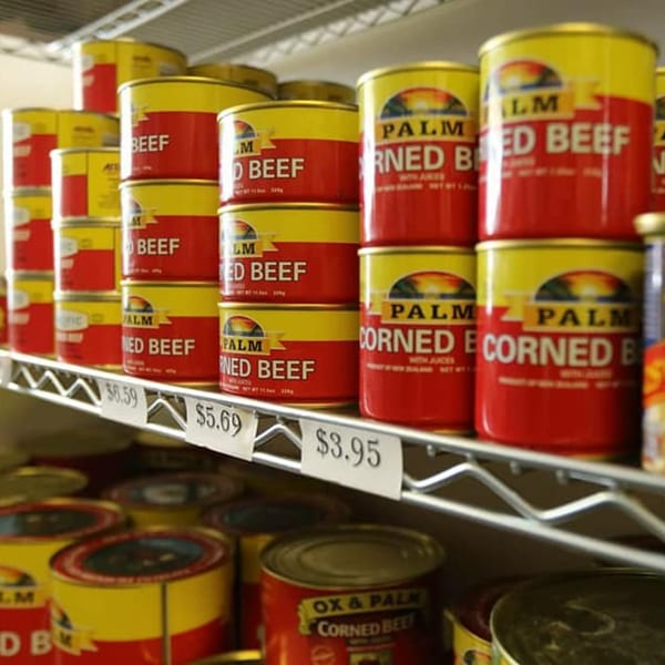 Shelves filled with red and yellow cans of Palm brand corned beef, priced for sale.