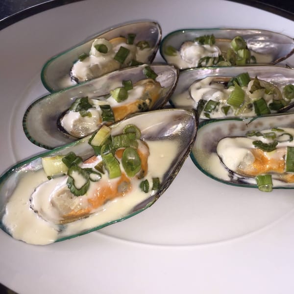 Polynesian mussels on a white plate, topped with creamy sauce and chopped green onions.