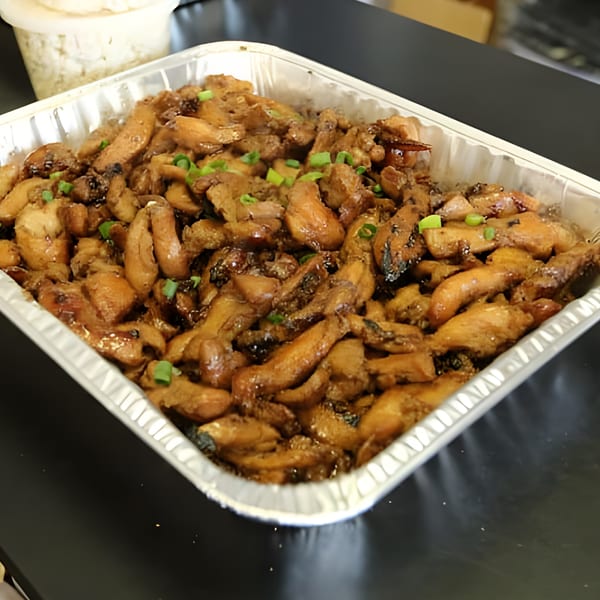 Polynesian chicken adobo with green onions in a foil pan, ready for catering.