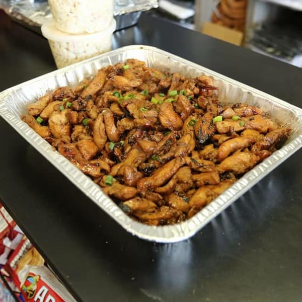 A large foil pan filled with Leilani's Polynesian Place teriyaki chicken, garnished with green onions.