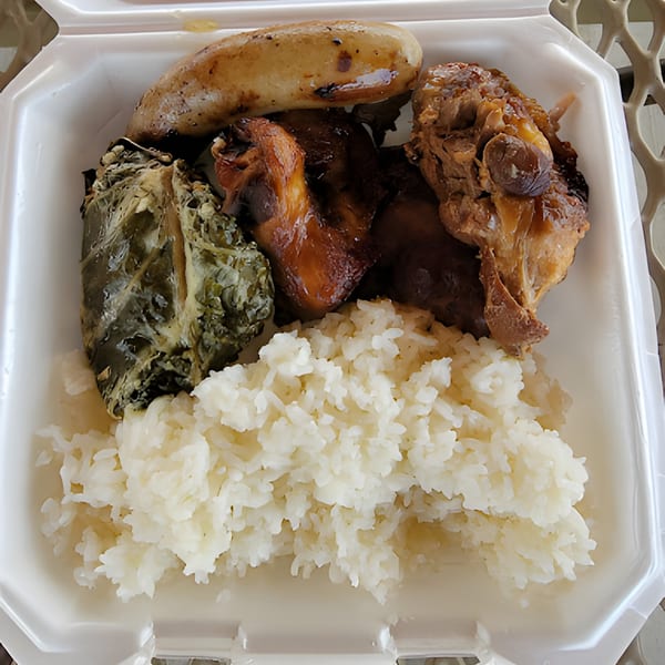 Polynesian plate lunch with rice, chicken, luau leaf, and a banana in a styrofoam container.